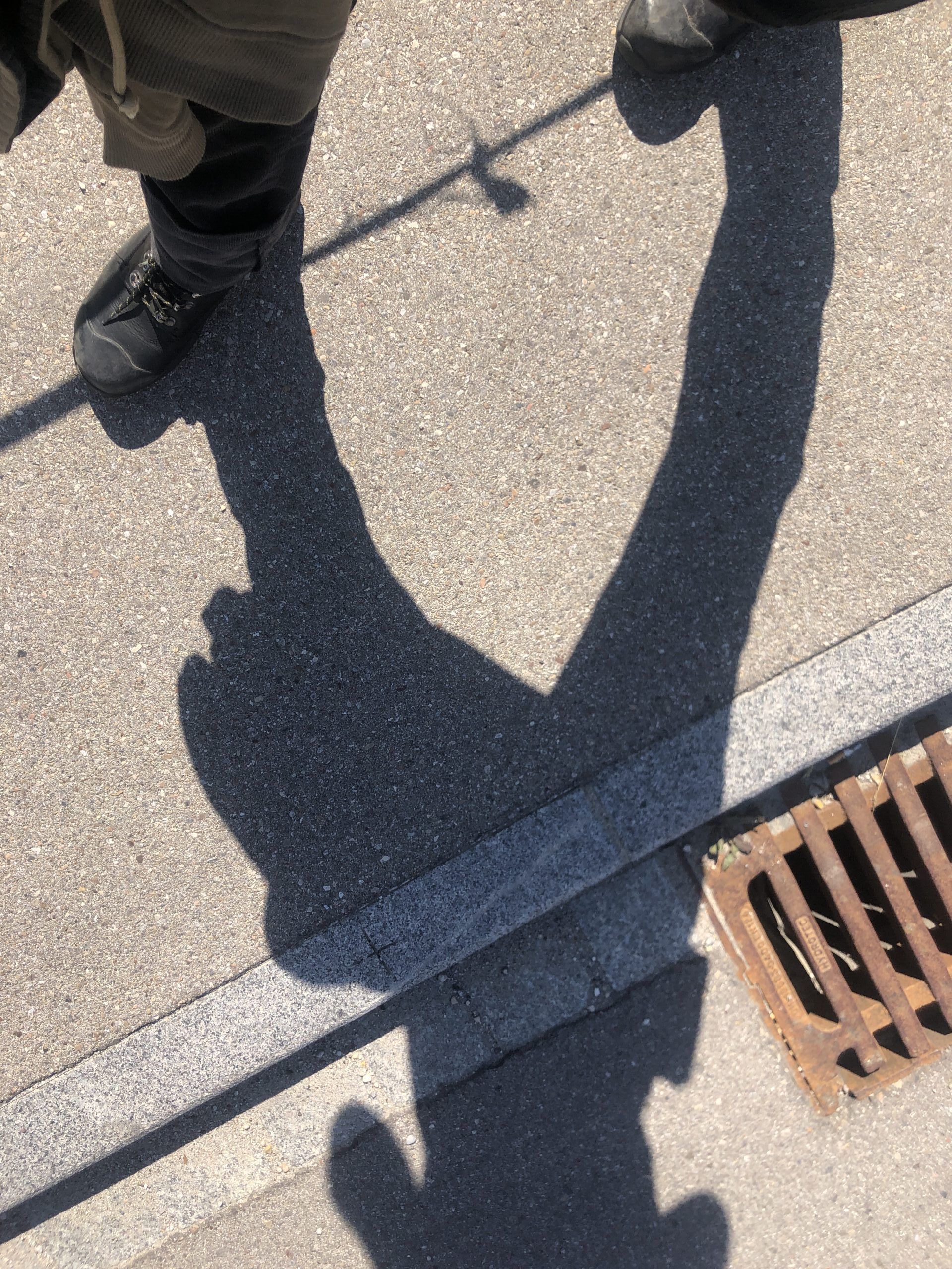 Bild von oben auf eine asphaltierte Straße. Gulli und Bordstein sind zu sehen und der Schatten eines Seil auf dem mein Schatten balanciert