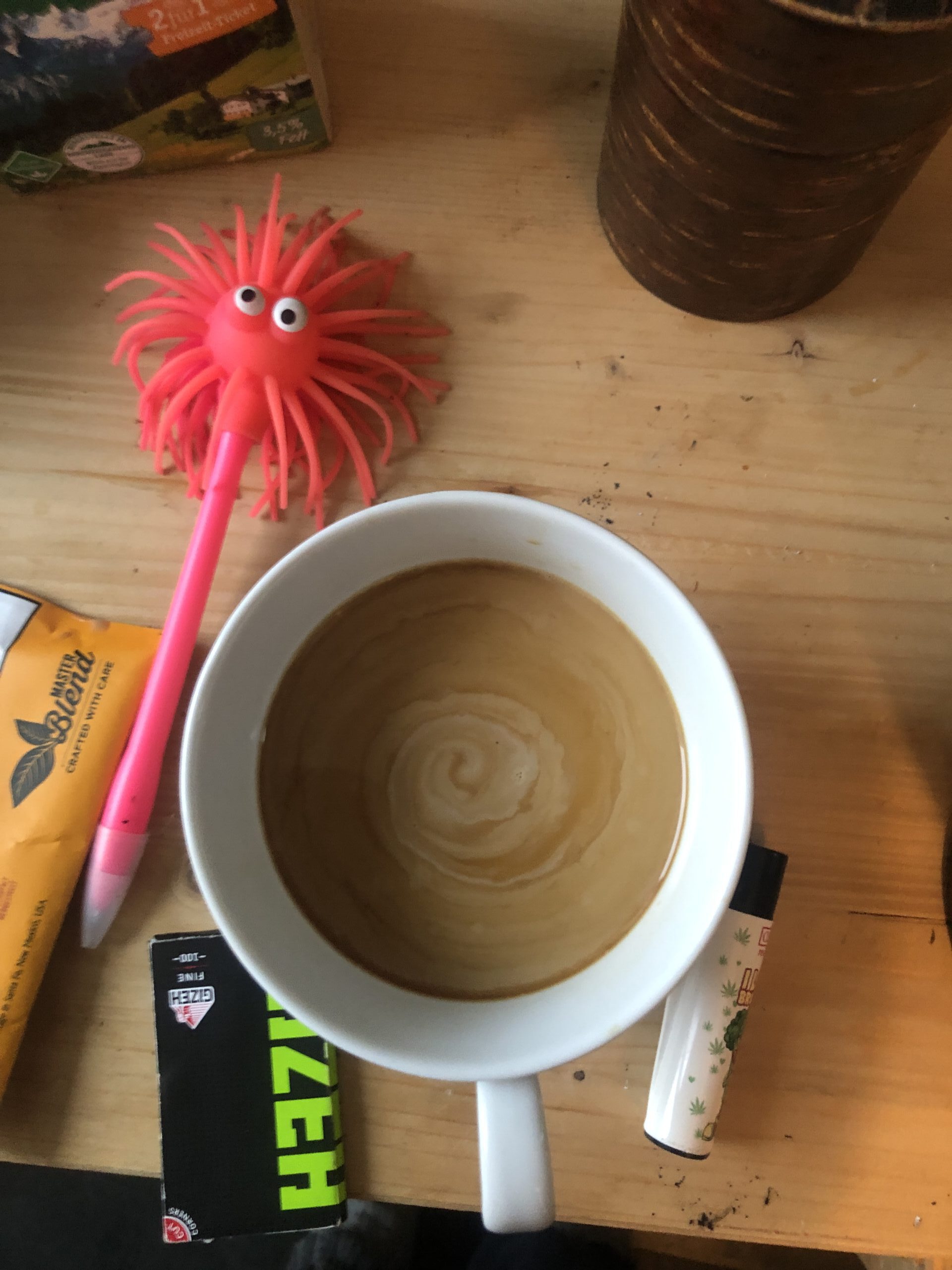 Bild von oben auf eine weisse Kaffeetasse. Auf dem Holztisch danebenDrehzeug und ein kurioser pinker Kugelschreiber