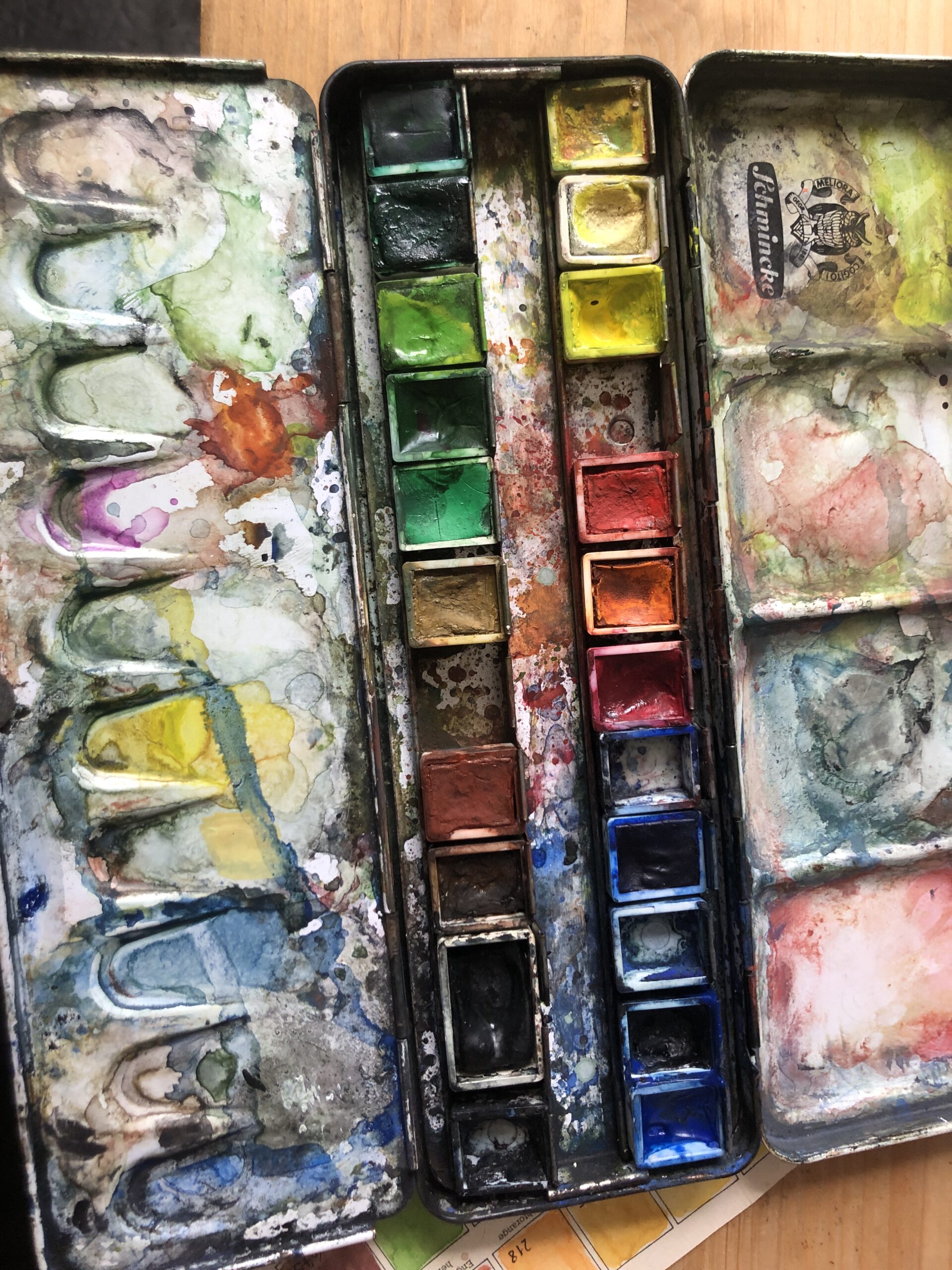 Ein benutzter Aquarellkasten, der Spuren von angemischten Farben zeigt